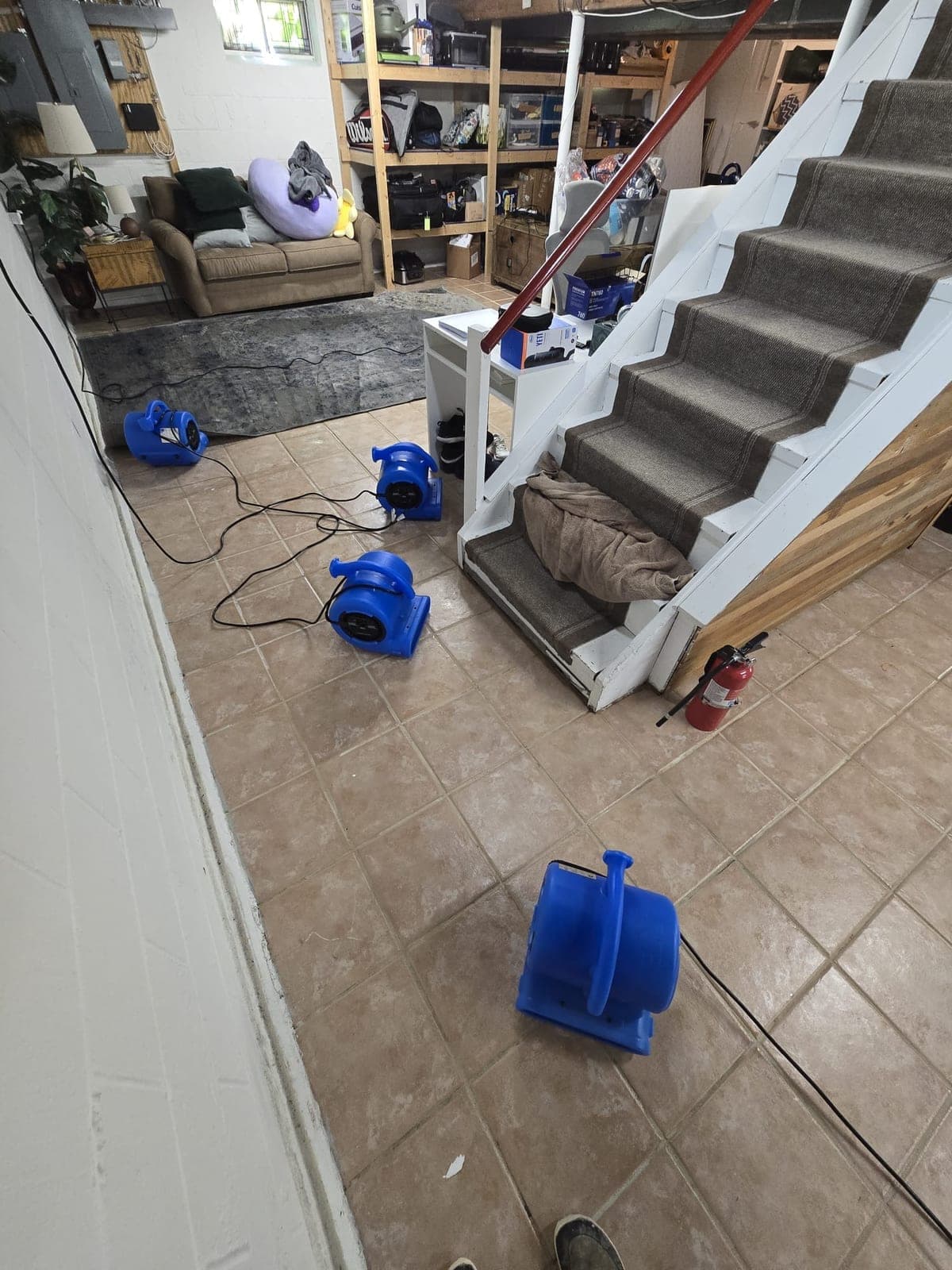 Four air movers drying a tiled basement floor beside a carpeted staircase in a Paterson NJ home
