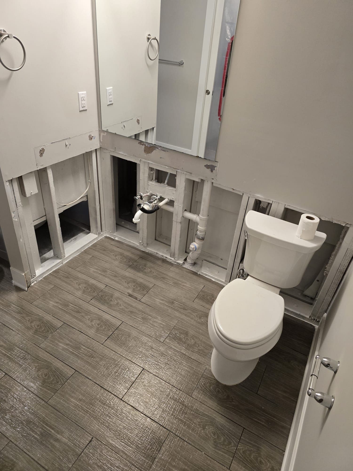 Bathroom with lower walls removed to the studs and plumbing exposed around an intact toilet during water mitigation