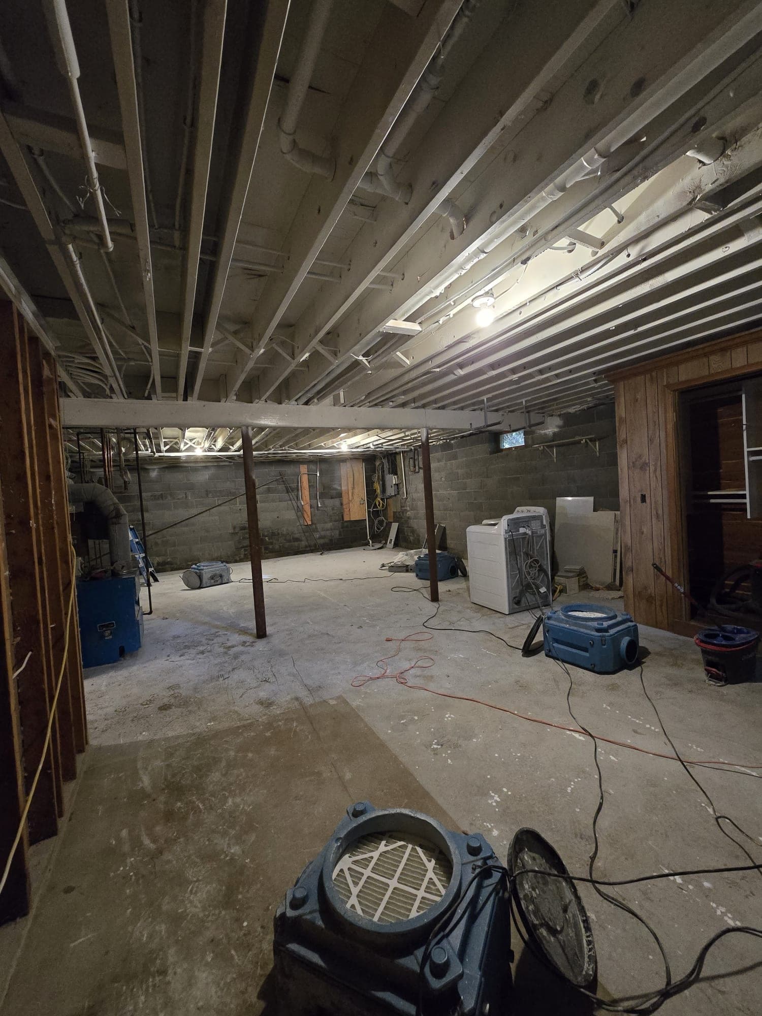 Blue air movers and dehumidification equipment spread across a gutted basement with exposed joists and block walls