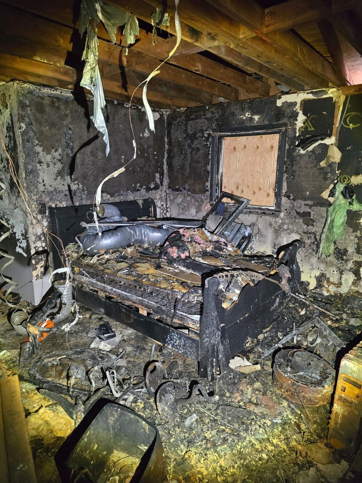 Fire-gutted bedroom in Hawthorne NJ with charred bed frame, burned mattress and soot-blackened walls