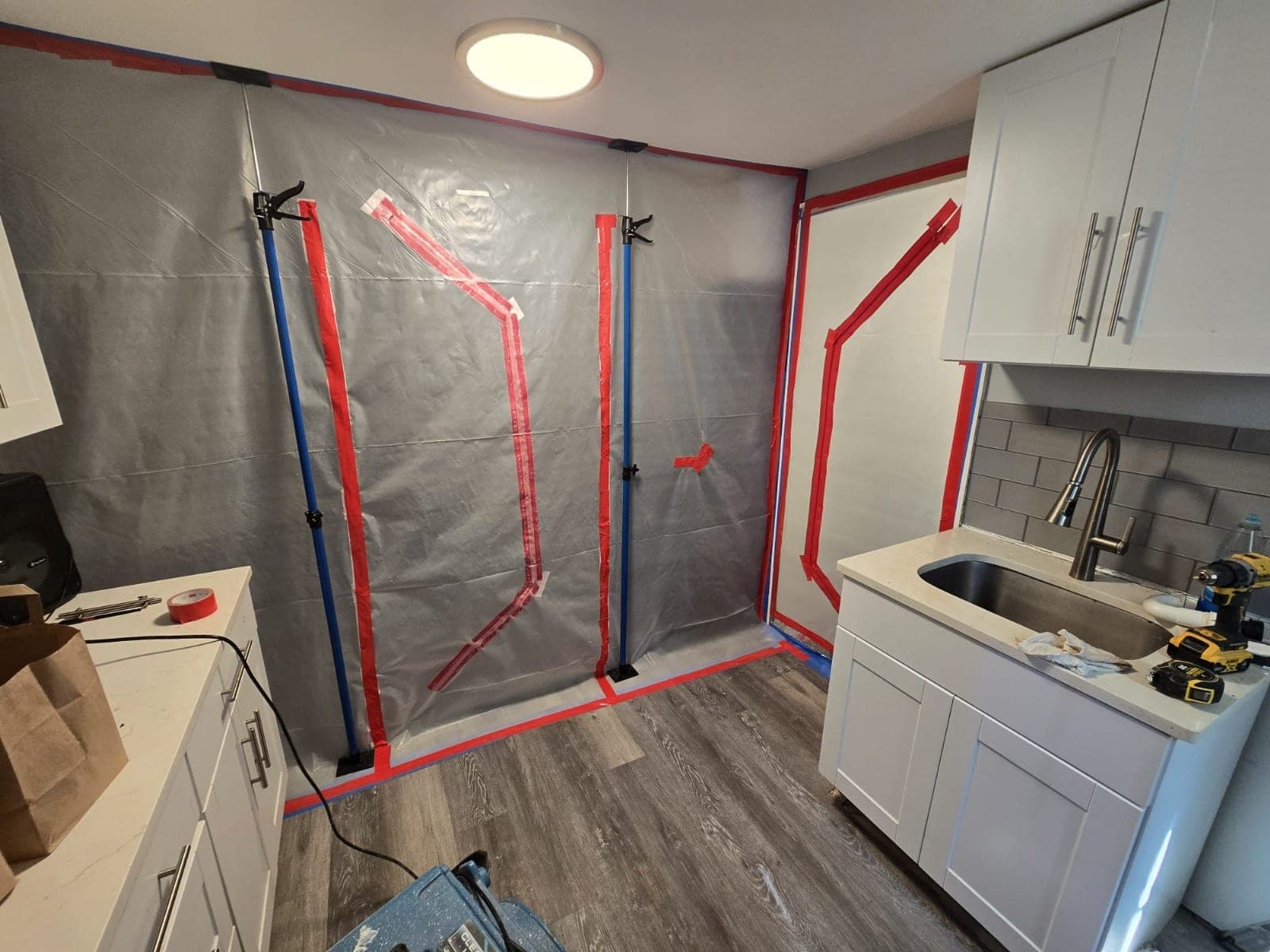 Plastic containment wall on spring-loaded poles with taped zipper seams sealing off part of a kitchen